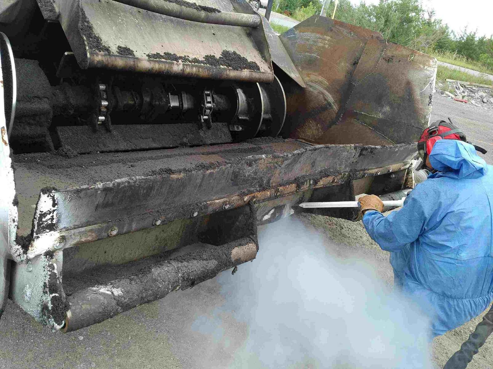 Opérateur en combinaison projetant de la glace carbonique pour décaper l’asphalte et le bitume d’un finisseur routier